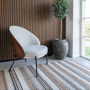 Modern chair against a slatted wood wall with a plant and striped rug.